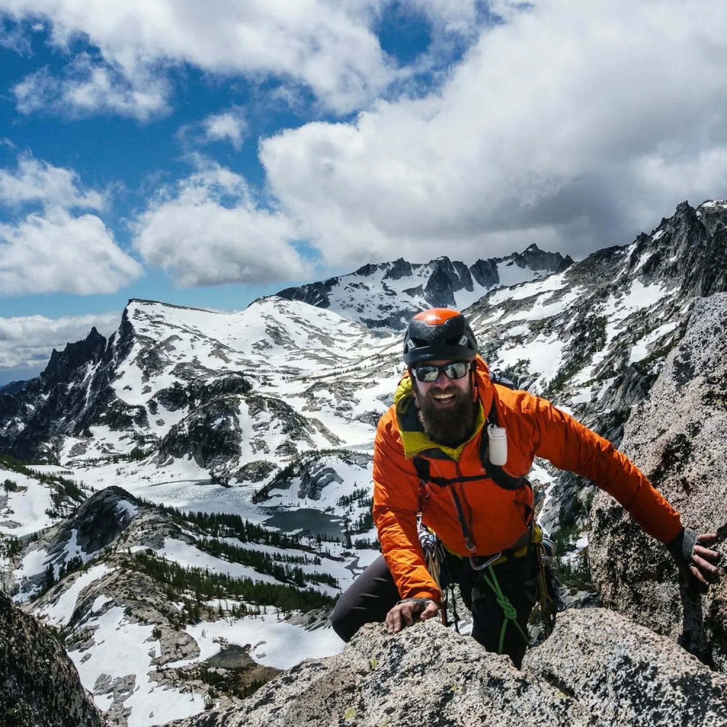 A climber in an orange jacket scrambling up a snowy ridge
