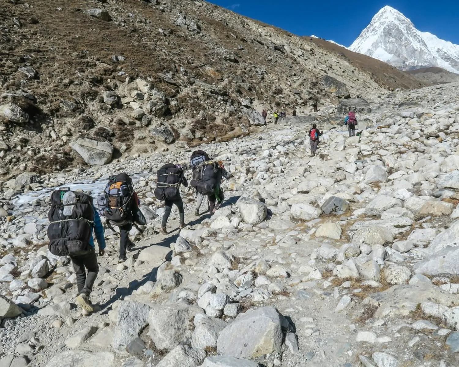 Guides trekking a rocky trail toward a snowy peak