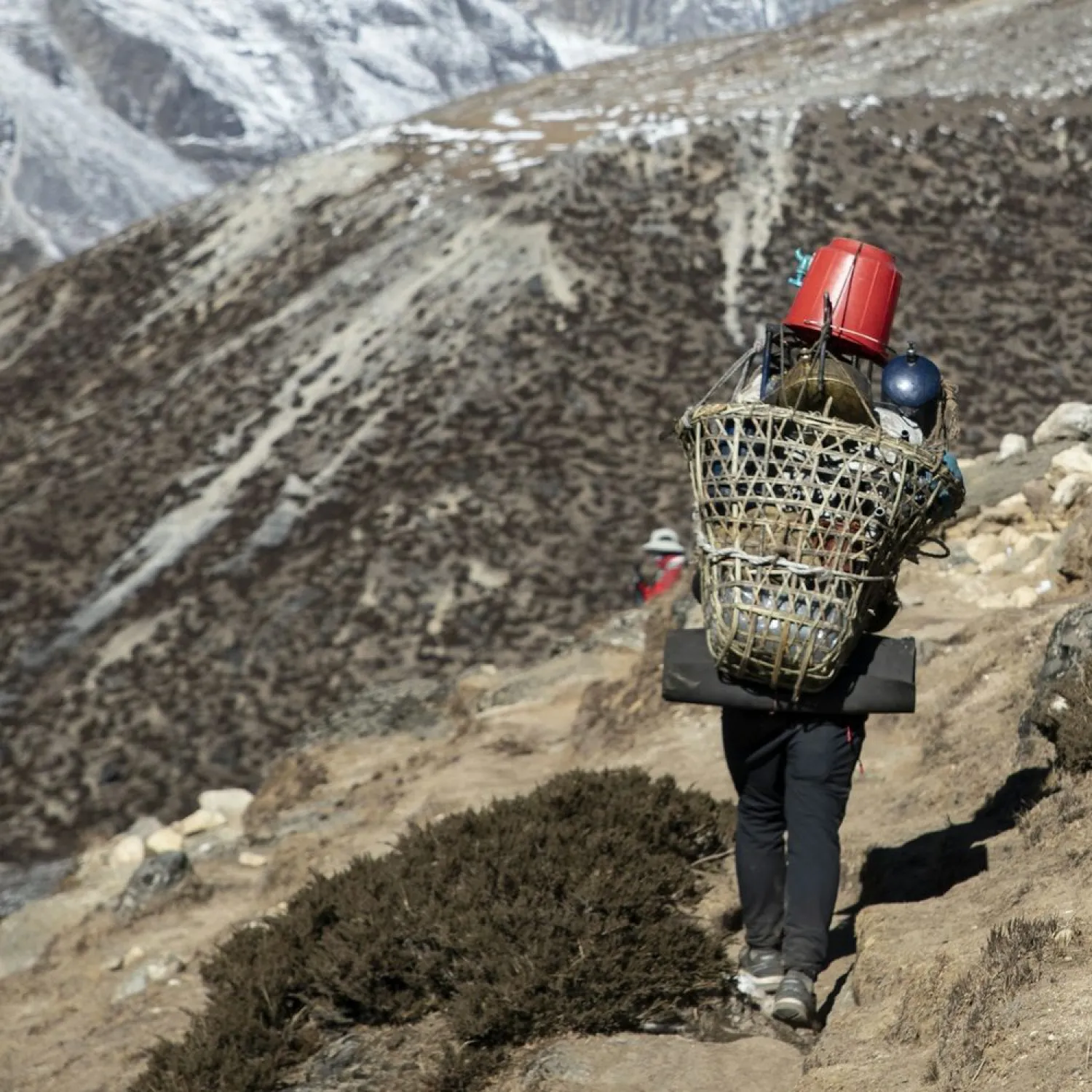 A porter carrying a basket load up a mountain trail