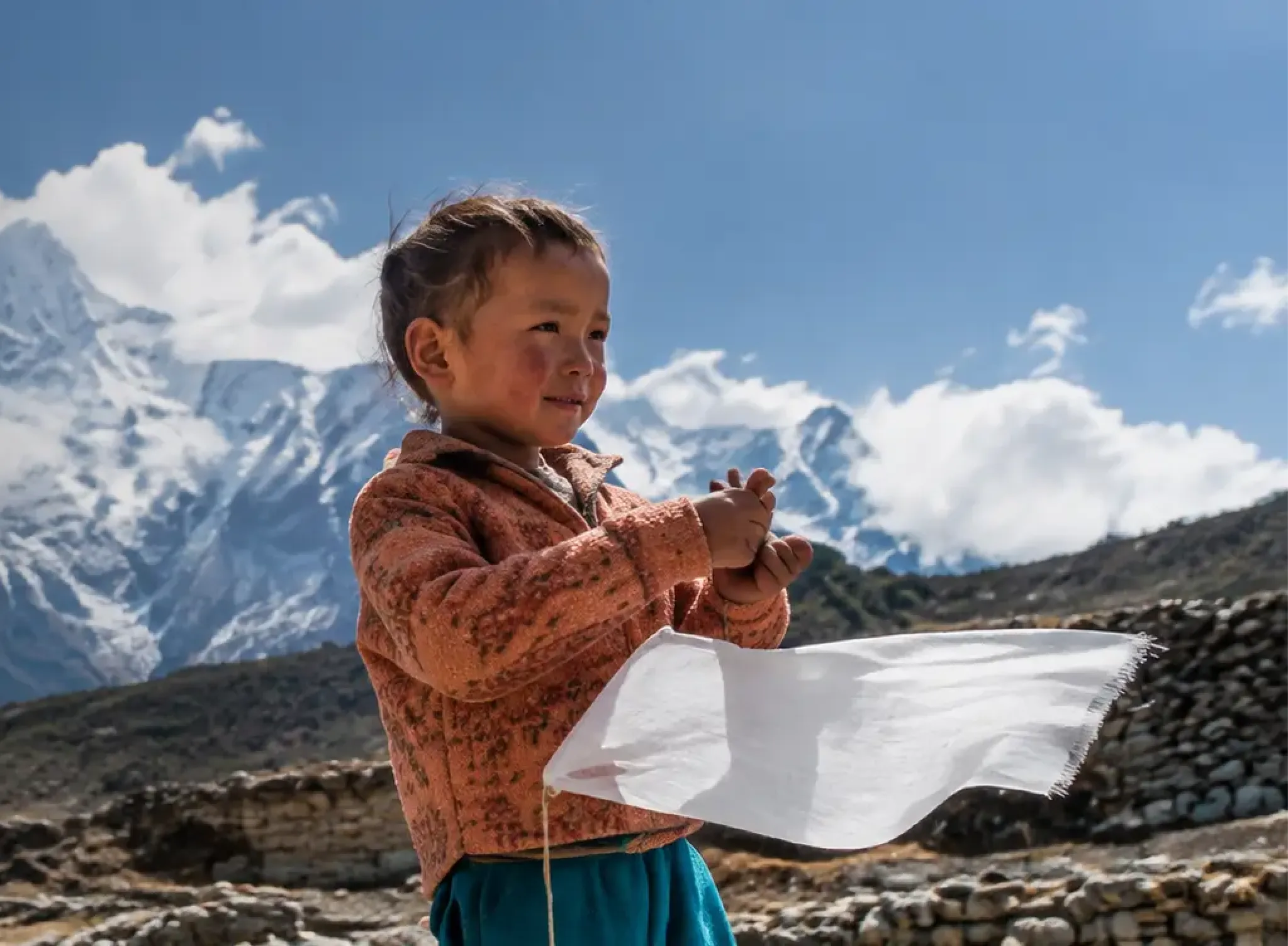 A child in a Himalayan village with snow-covered mountains behind them